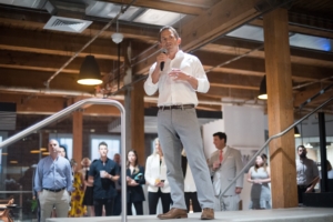 man in white button down and slacks speaks to group of business people at event space
